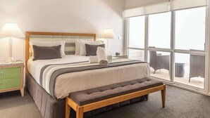 Ein Schlafzimmer mit einem großen Bett, Nachttischlampen, einer Bank und Blick durch ein großes Fenster.