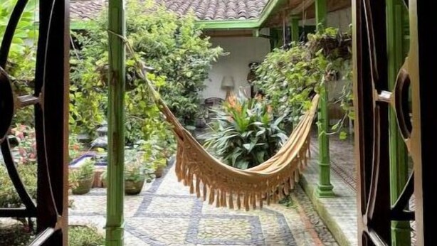 An entrance with a wrought iron gate, a hammock, and a tiled pathway leading to a building with a tiled roof.