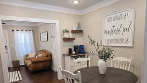 A dining area with a round table and white chairs, a brown leather sofa, and a white vase with a plant. - Easy Living In Delightful Duplex (Lubbock)