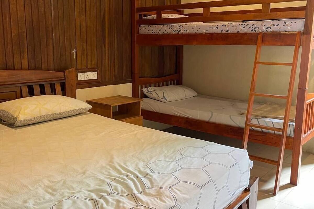 A bunk bed with a ladder, a bedside table, and a wooden wardrobe in a room with tiled flooring.