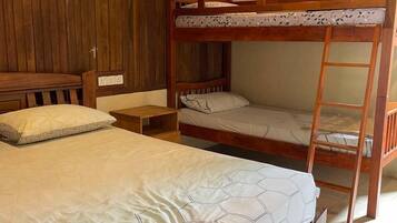 A bunk bed with a ladder, a bedside table, and a wooden wardrobe in a room with tiled flooring.
