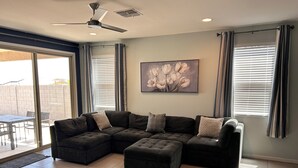 Una sala de estar con un sofá modular, un ventilador de techo y un ventanal con persianas.