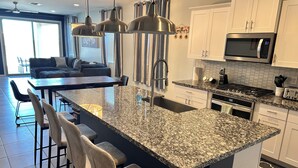 Une cuisine moderne dotée de plans de travail en granit, d’appareils électroménagers en acier inoxydable et d’un îlot central avec des tabourets de bar.