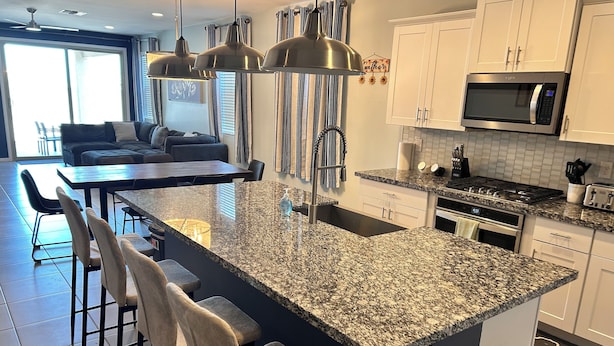 Una cocina moderna con encimeras de granito, electrodomésticos de acero inoxidable y una isla central con taburetes de bar.