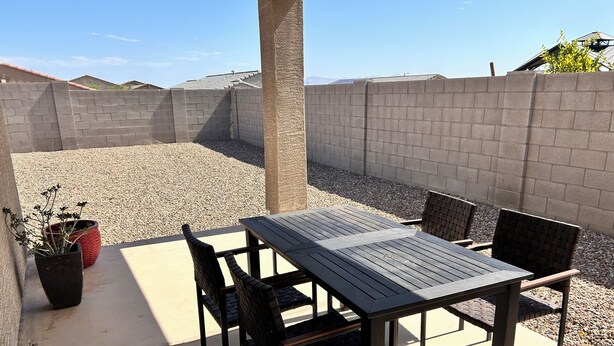 Une terrasse avec une table et des chaises, entourée d’un mur en béton et d’une zone recouverte de gravier.