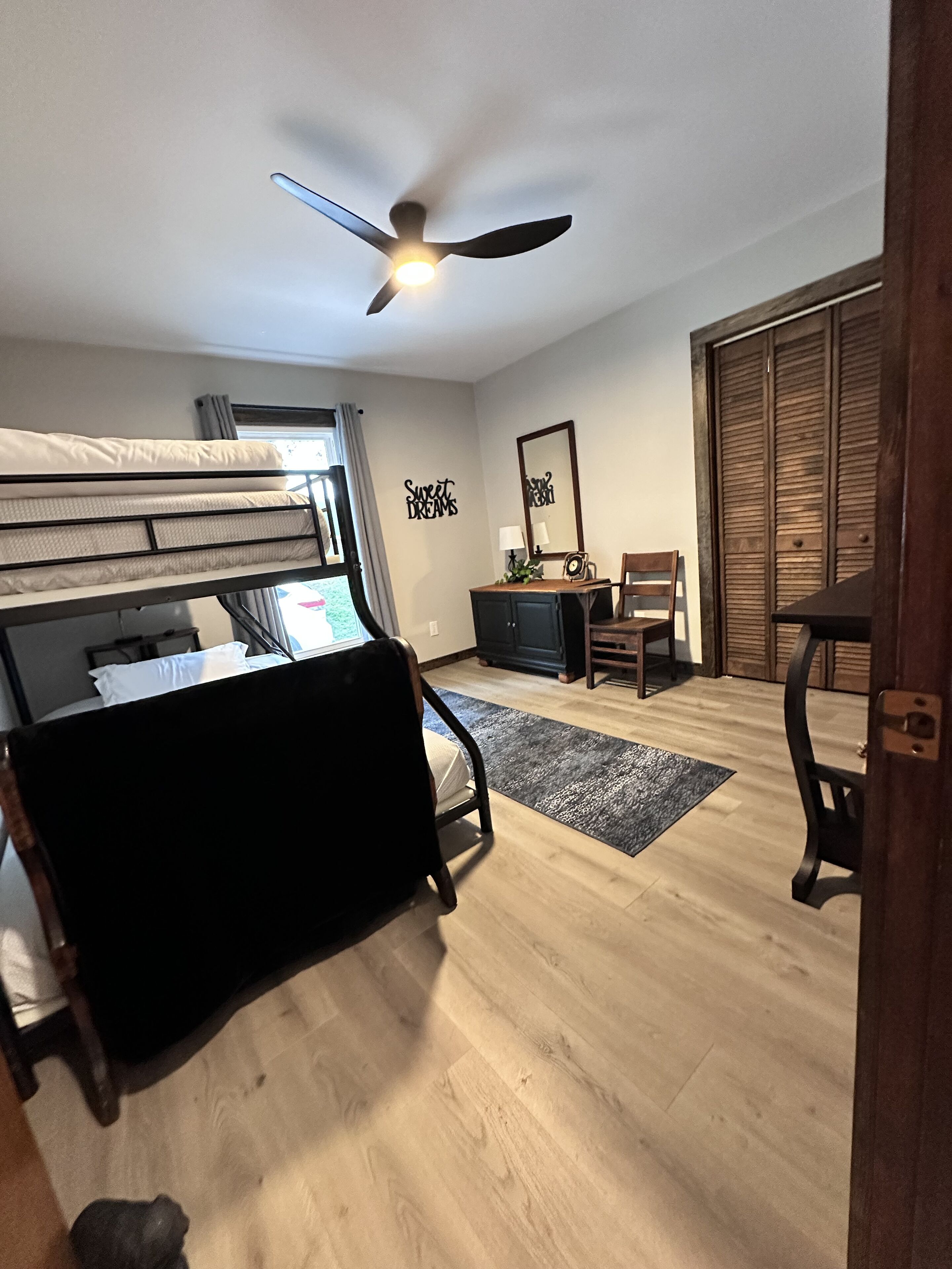 A bedroom with a bunk bed, a desk with a chair, a ceiling fan, and a wardrobe.