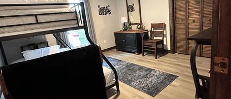 A bedroom with a bunk bed, a desk with a chair, a ceiling fan, and a wardrobe.