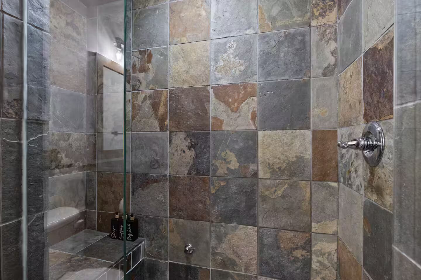 Una zona de ducha con azulejos de piedra y un panel de vidrio.