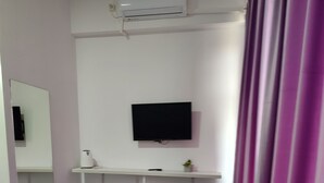 A hotel room with a bed, a desk, a chair, a TV, a mirror, a heater, and a curtain.
