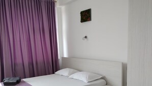 A neatly made bed with a white headboard, a purple bedspread, and a small bedside table.