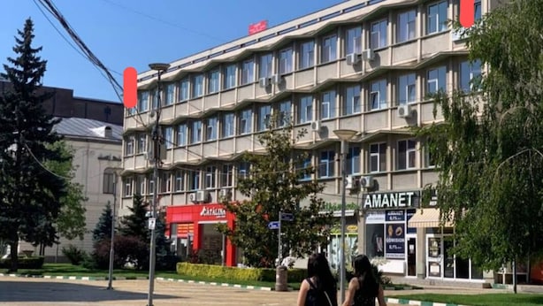 A multi-story building with a row of windows and a red sign on the ground floor.