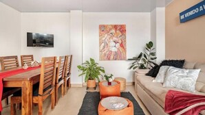 A modern living room with a wooden dining table, chairs, a sofa, and a TV mounted on the wall. - Comfortable and spacious apartment in Usaquén Bogotá (Bogotá, D.C.)