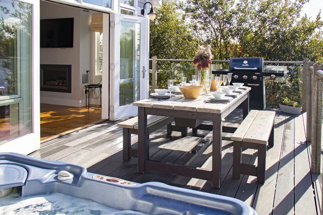 Une terrasse extérieure avec une table en bois dressée pour les repas, un barbecue et un jacuzzi.