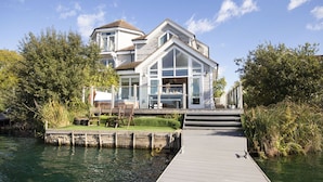 A waterfront house with a dock, a grassy deck, and a large glass window. - The Landings 18, Waters Reach (P) - Lakeside Luxury, Hot Tub, Tennis, Sleeps 10 (South Cerney)