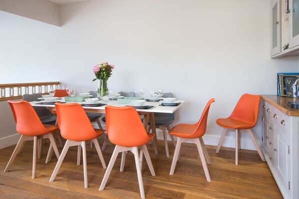 A dining area with a wooden table set for six, surrounded by six orange chairs.