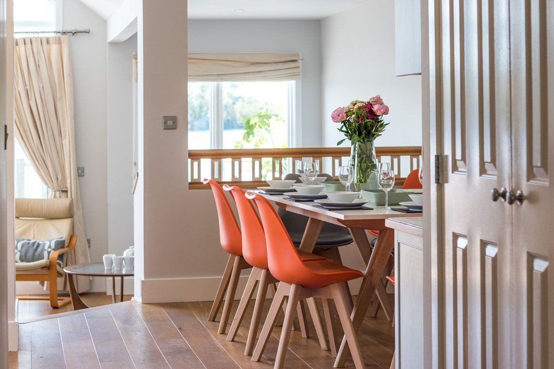 A dining area with a wooden table, orange chairs, and a vase of flowers.