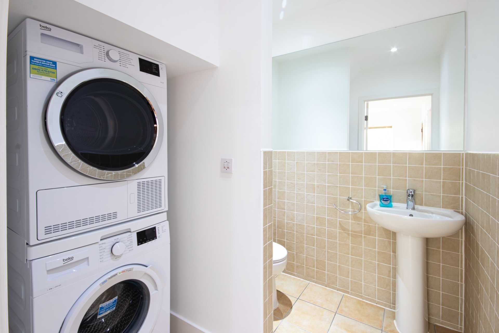 A laundry area with a front-loading washer and dryer, a sink with a mirror above it, and a toilet.