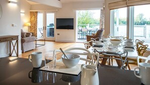 Een moderne eetruimte met een tafel voor vier personen, een bank en een televisie op de achtergrond.
