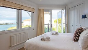 Een slaapkamer met een groot bed, uitzicht op zee en een raam met gordijnen.