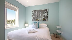 Ein Schlafzimmer mit Bett, Fenster, Stadtbildgemälde und Mülleimer.