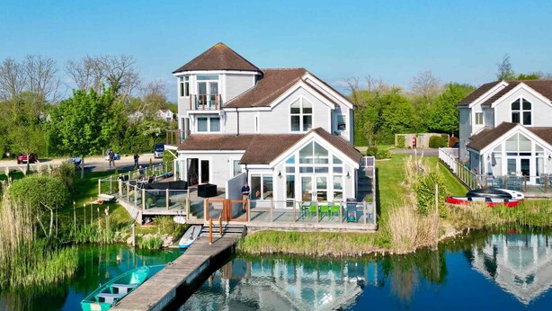 Ein zweistöckiges Haus mit Balkon und einer Anlegestelle, die sich in ruhiges Wasser erstreckt.