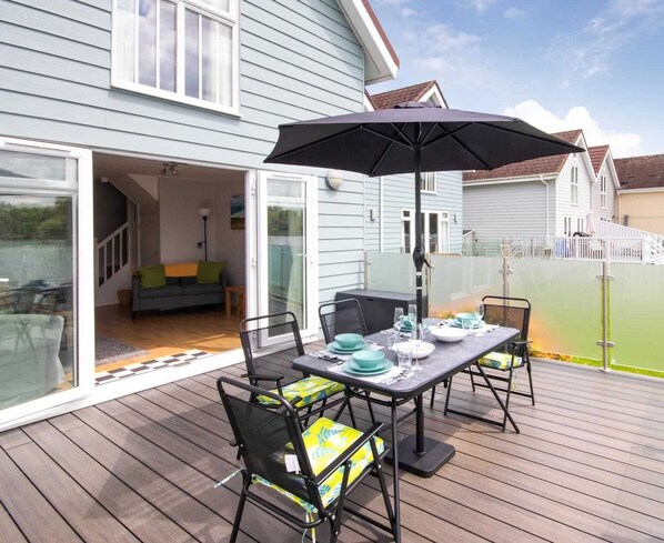 Een terras met een eettafel, buitenmeubels en een overdekt gedeelte met een parasol.