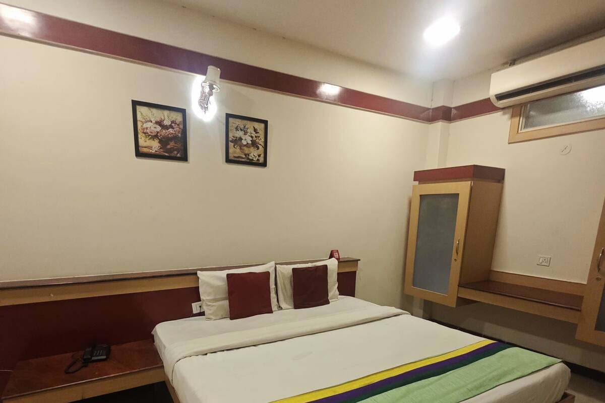 A hotel room with a bed, a bench, a wardrobe, and two wall-mounted pictures.