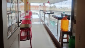 A modern interior with a long corridor leading to a balcony. There are tables and chairs along the corridor, and a large window on the balcony offers a view of the street. - Span Suites by Stayz Royale (Bengaluru)