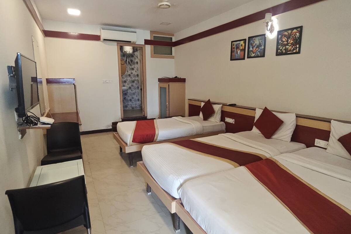 A hotel room with three beds, a desk, a chair, and a ceiling fan.