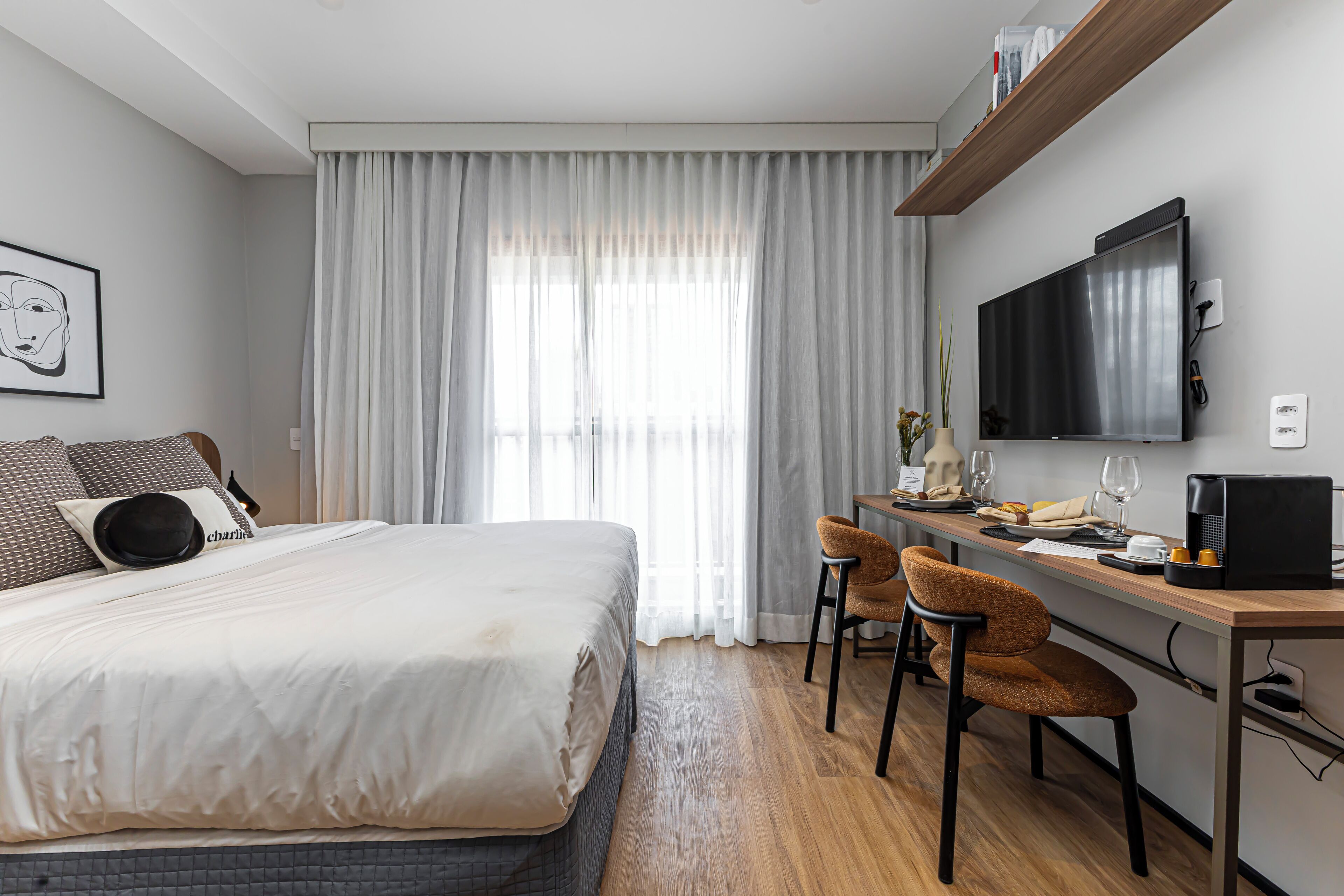 A hotel room with a bed, a desk with two chairs, a television, and a window with curtains.