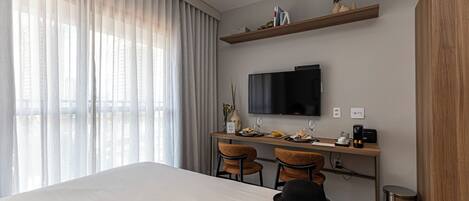 Habitación de hotel con cama, escritorio, dos sillas, televisor y un pequeño cubo de basura.