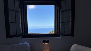 Une chambre avec une fenêtre donnant sur la mer, une lampe de chevet et deux lits avec des oreillers.