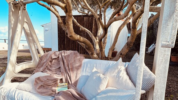 Un hamac tendu sous un arbre, avec un livre et une couverture à l’intérieur.