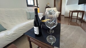 Un salon avec un canapé blanc, une table noire sur laquelle se trouvent une bouteille de vin et un verre, et un téléviseur fixé au mur.