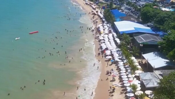 A beach with people swimming and sunbathing, umbrellas, and beachside buildings.