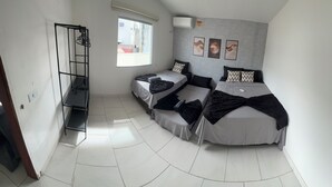 A small, well-lit room with two single beds, a standing shelf unit, and a window providing natural light.