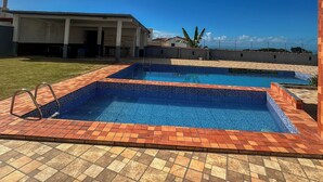 A swimming pool with a tiled deck, a clear sky, and a building in the background.