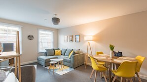 A modern living room with a grey sofa, yellow chairs, a dining table, and a lamp.