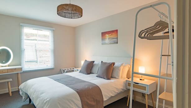 A bedroom with a bed, bedside table, lamp, and a wall-mounted rack.