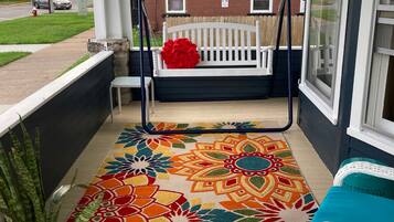 A porch with a colorful rug, a white bench, and a potted plant.