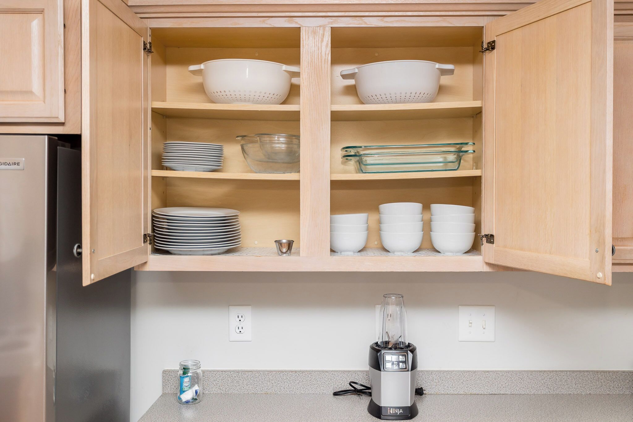 A kitchen with wooden cabinets, a blender on the counter, and various kitchenware including bowls and plates.