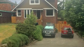 Une maison à deux étages, avec une façade en briques, un porche à l’avant et une allée où sont garées deux voitures.
