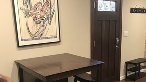 Un coin repas avec une table en bois foncé et des chaises assorties, une affiche encadrée au mur, une porte avec une fenêtre et une petite table d’appoint.