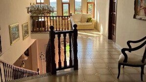 Una habitación amplia con techo alto, ventanas grandes, escalera y candelabro.