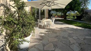 Un patio con suelo de piedra, mobiliario exterior y un amplio paraguas que da sombra.