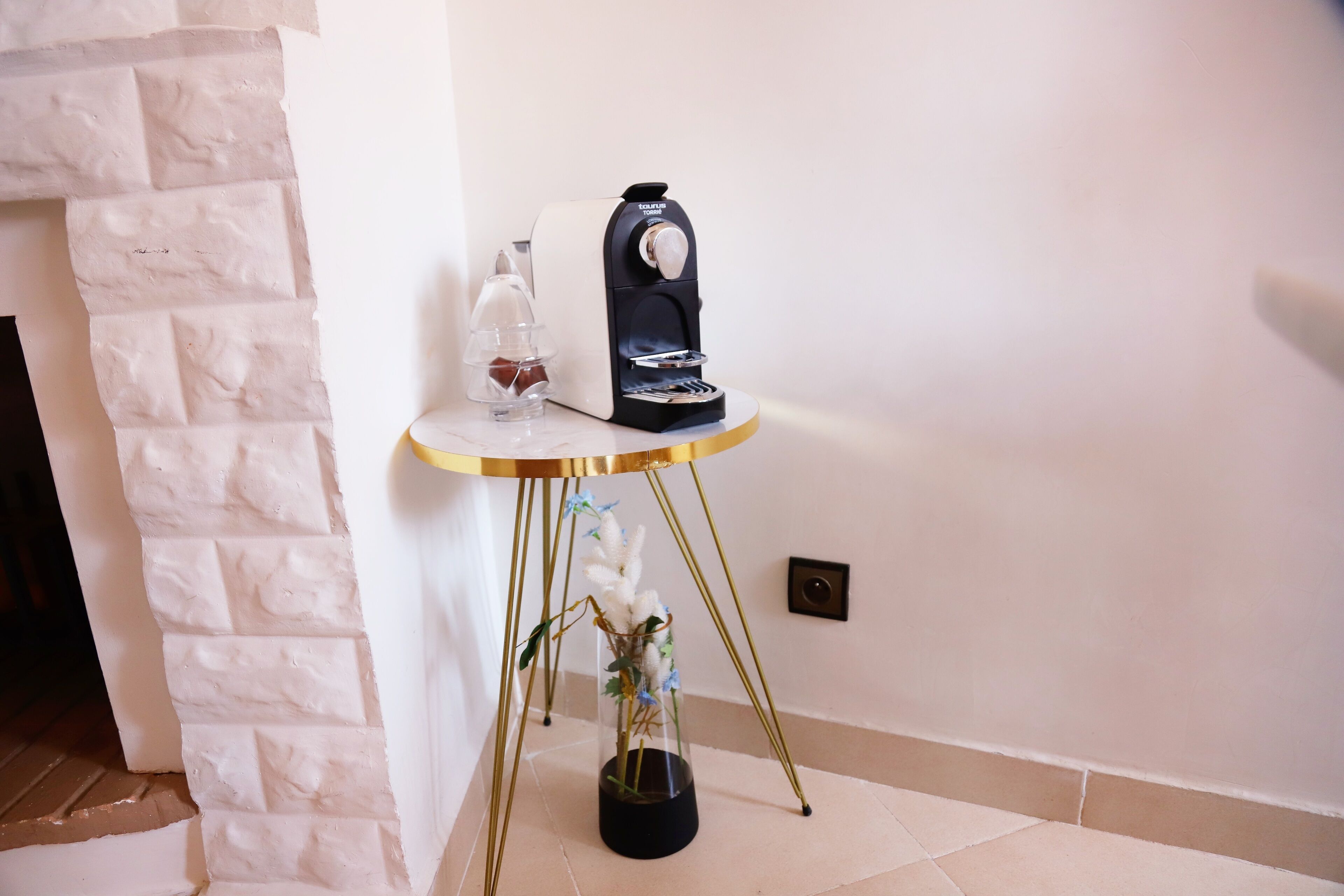 Uma mesa redonda pequena com uma máquina de café e um copo de vinho tinto.