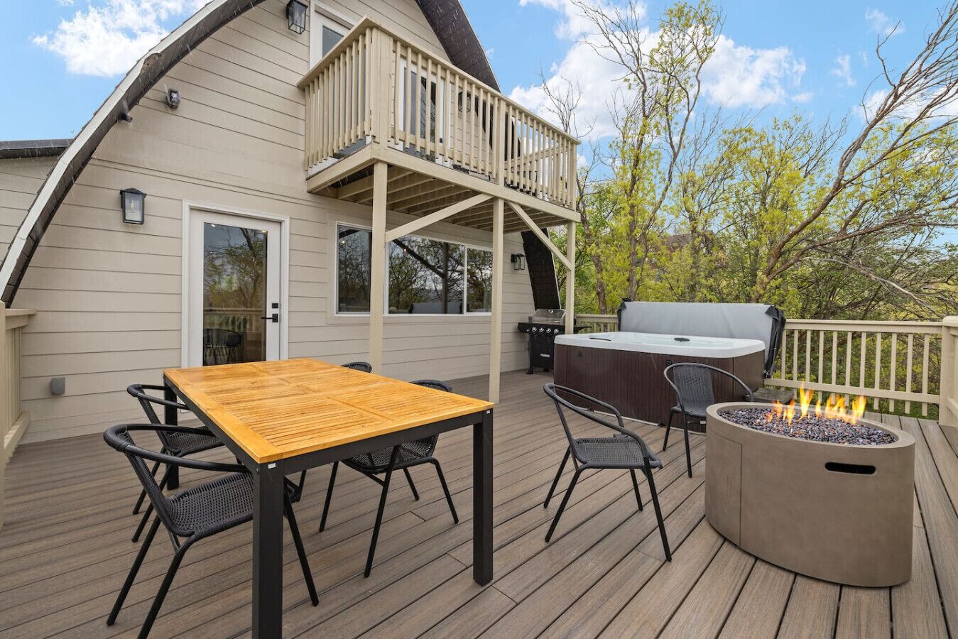 Eine Terrasse mit Holztisch und -stühlen, einem Grill, einem Whirlpool und einer Feuerstelle.