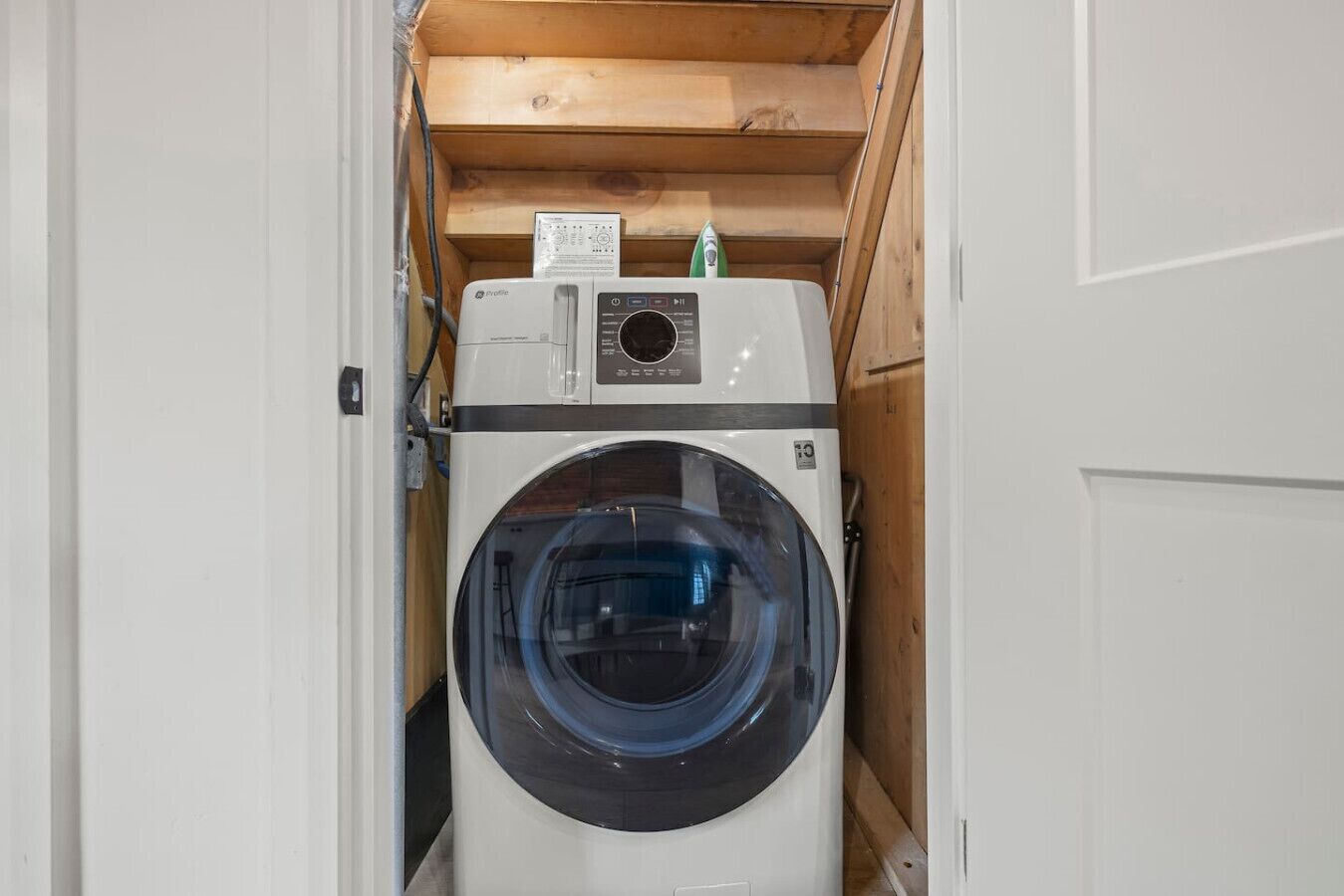 Eine kompakte, weiße Waschmaschine in einem rustikalen Hauswirtschaftsraum mit Holzboden und -decke.