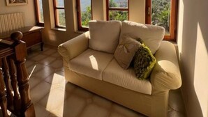 Un salon avec un canapé beige, de grandes fenêtres et une vue sur la verdure.