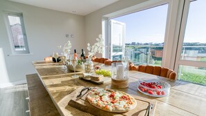 A dining area with a wooden table, a pizza, and a view of the outdoors. - Garreg Hen -  a sea view that sleeps 8 guests  in 4 bedrooms (Trearddur Bay)